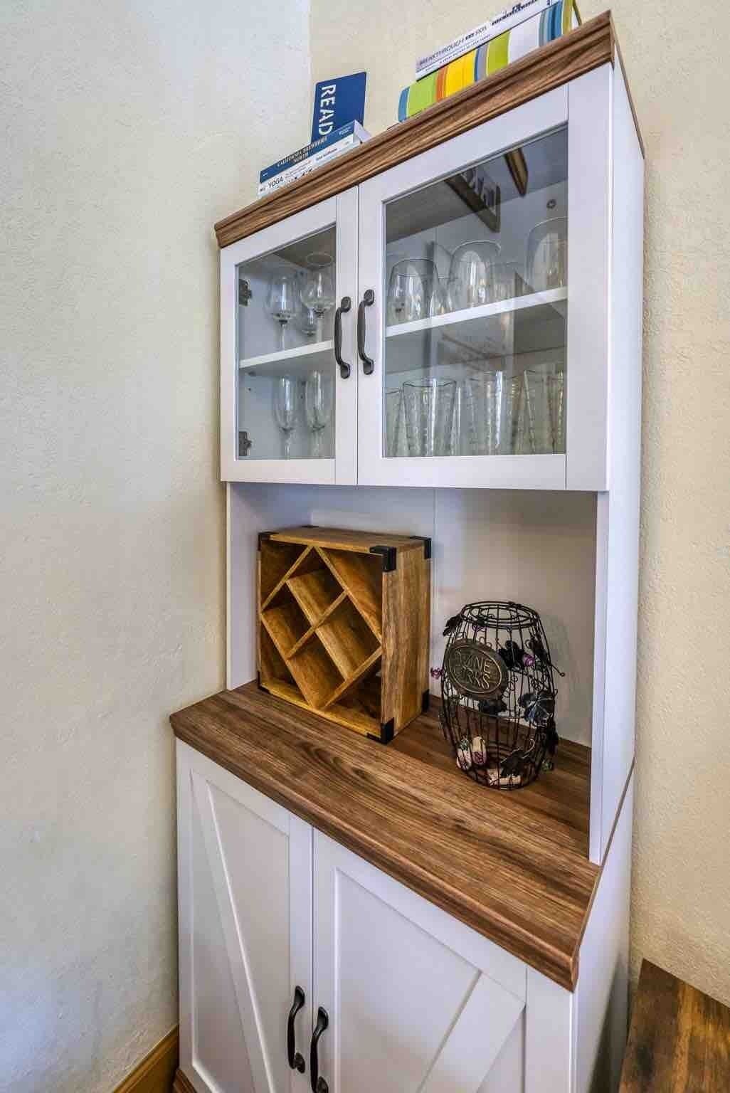 A kitchen with white cabinets, a wooden countertop, and a glass cabinet above containing glassware.