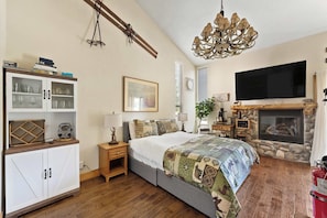 Une chambre à coucher comprenant un lit, une télévision, une cheminée, une armoire aux portes vitrées et un lustre.