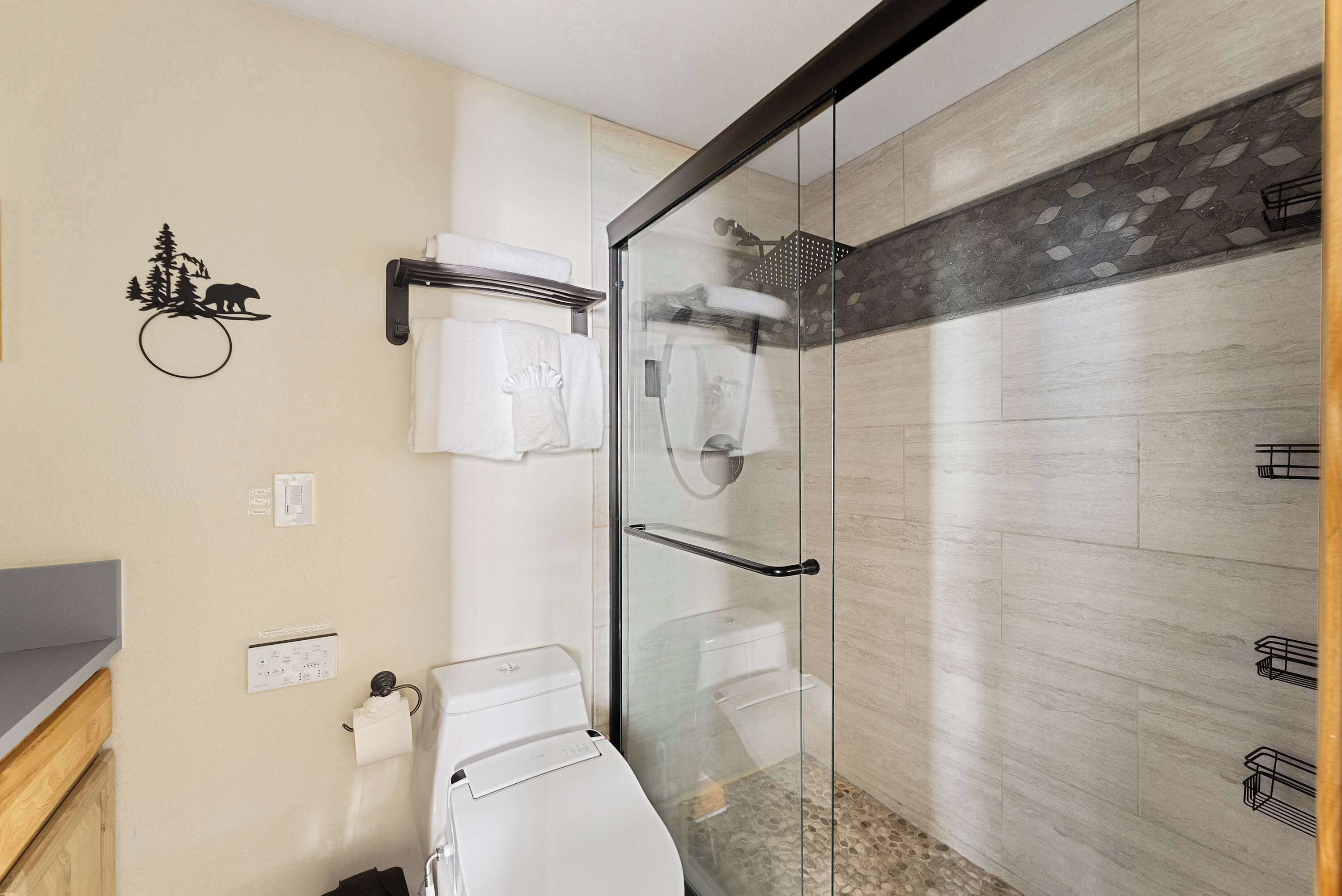 Un baño moderno con cabina de ducha de vidrio, inodoro, toallero y un elemento decorativo en la pared.