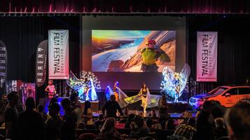 A stage with a large screen displaying a mountainous landscape, performers in costumes, and banners for the Tahoe Adventure Film Festival.