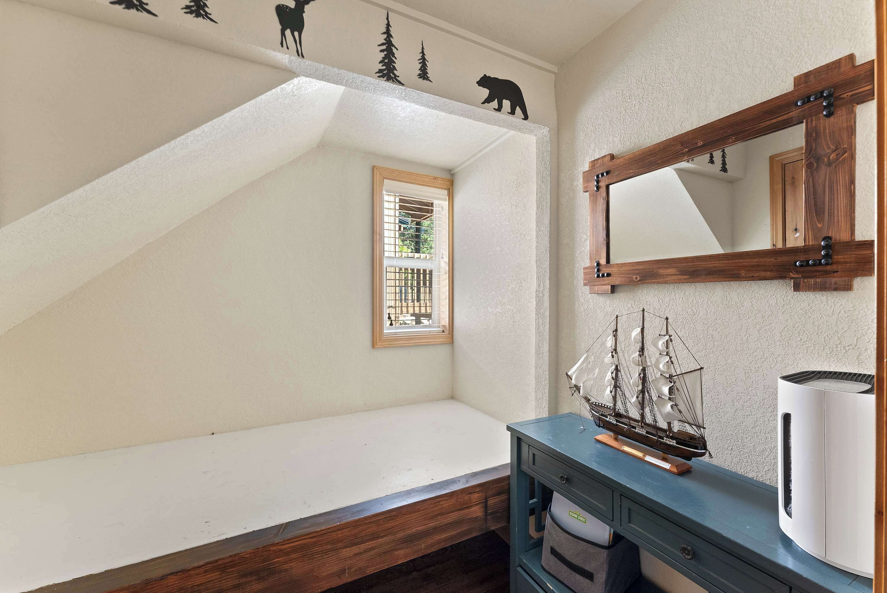 A room with a sloped ceiling, a window with a metal grill, a wooden bench, a ship model, and a white appliance.