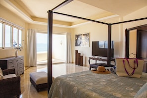 A four-poster bed with a view of the beach, a television, and a desk with a chair.