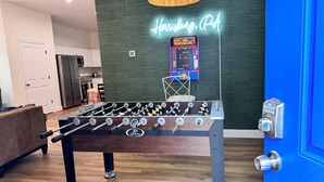 Un tavolo da calcio in una stanza con un neon che riporta la scritta "Harrisburg, PA" sulla parete, una zona cucina sullo sfondo e una porta blu alla destra.