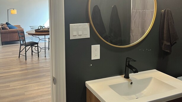 Un bagno moderno con uno specchio rotondo, un lavandino bianco e un rubinetto nero. Sopra lo specchio c'è un lampadario e un asciugamano appeso al muro.