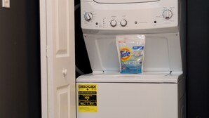 Una lavatrice a carica frontale con una confezione di detersivo Tide sopra, accanto a una porta bianca e un secchio.