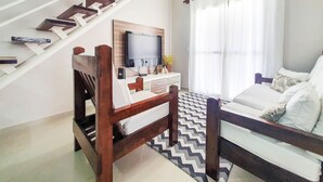 Un salon moderne avec un escalier, un téléviseur à écran plat, un bureau avec un ordinateur, un lit avec une literie blanche et un tapis à motifs.