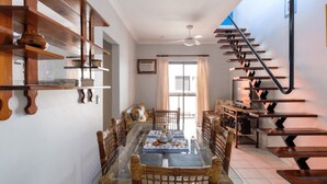 Un coin repas avec une table en verre, des chaises en osier et un escalier doté d’une rampe noire.