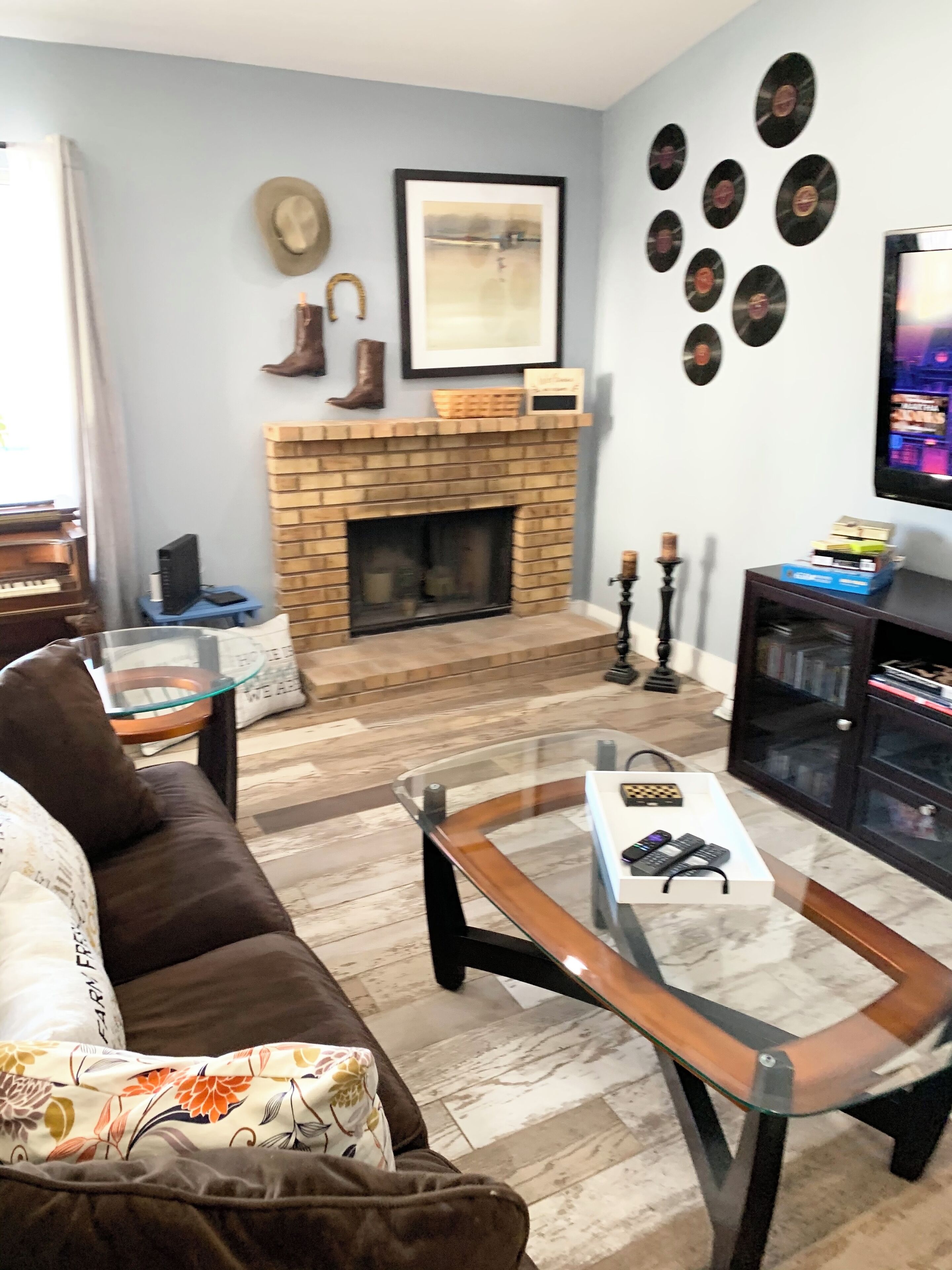 A living room with a brown sofa, a glass coffee table, a fireplace, and a wall decorated with vinyl records.