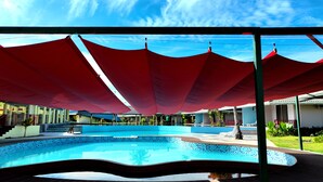 A swimming pool with a red canopy overhead, surrounded by buildings and greenery.