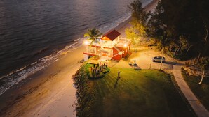 A beachfront property with a red-roofed building, a grassy area, and a paved path leading to the beach.