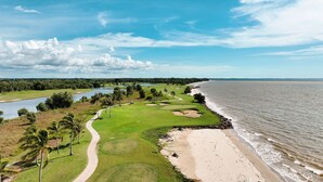 A coastal golf course with a sandy beach, a water body, and a path leading to the beach.