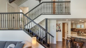 A spacious living area with a staircase, a kitchen with bar stools, and a cozy seating area with a lamp. - Large West Vail Home - Hot Tub & Ski Lockers (Vail)