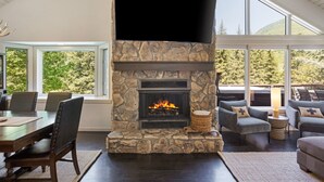 A stone fireplace with a flat-screen TV above it, a dining area with chairs, and a seating area with sofas and a lamp. - Large West Vail Home - Hot Tub & Ski Lockers (Vail)