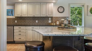 A kitchen with white cabinets, a brick backsplash, a clock, and a window with a view of trees. - Large West Vail Home - Hot Tub & Ski Lockers (Vail)
