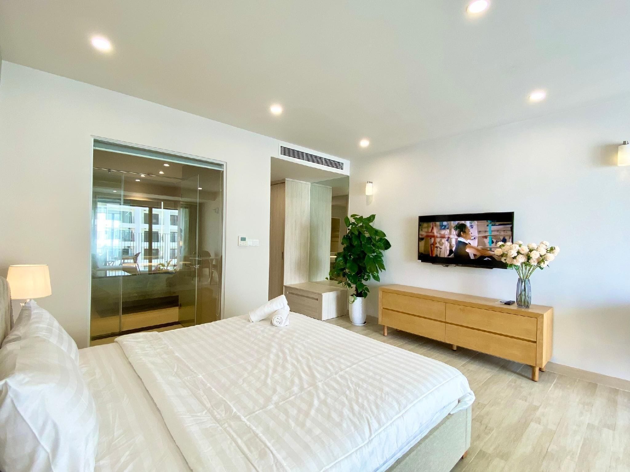 Quarto moderno com uma cama grande, televisão, cómoda de madeira e uma planta.