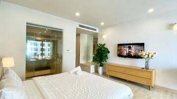 Quarto moderno com uma cama grande, televisão, cómoda de madeira e uma planta.