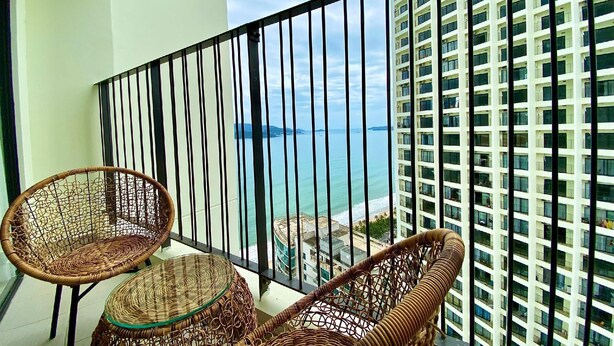 A balcony with wicker furniture and a view of a high-rise building and the sea. - Wise Stay Gold Coast Apartment (Nha Trang)