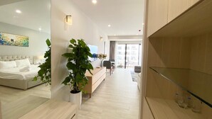 A modern hotel room with a bed, a large mirror, a potted plant, a wooden cabinet, and a glass shelf. - Wise Stay Gold Coast Apartment (Nha Trang)