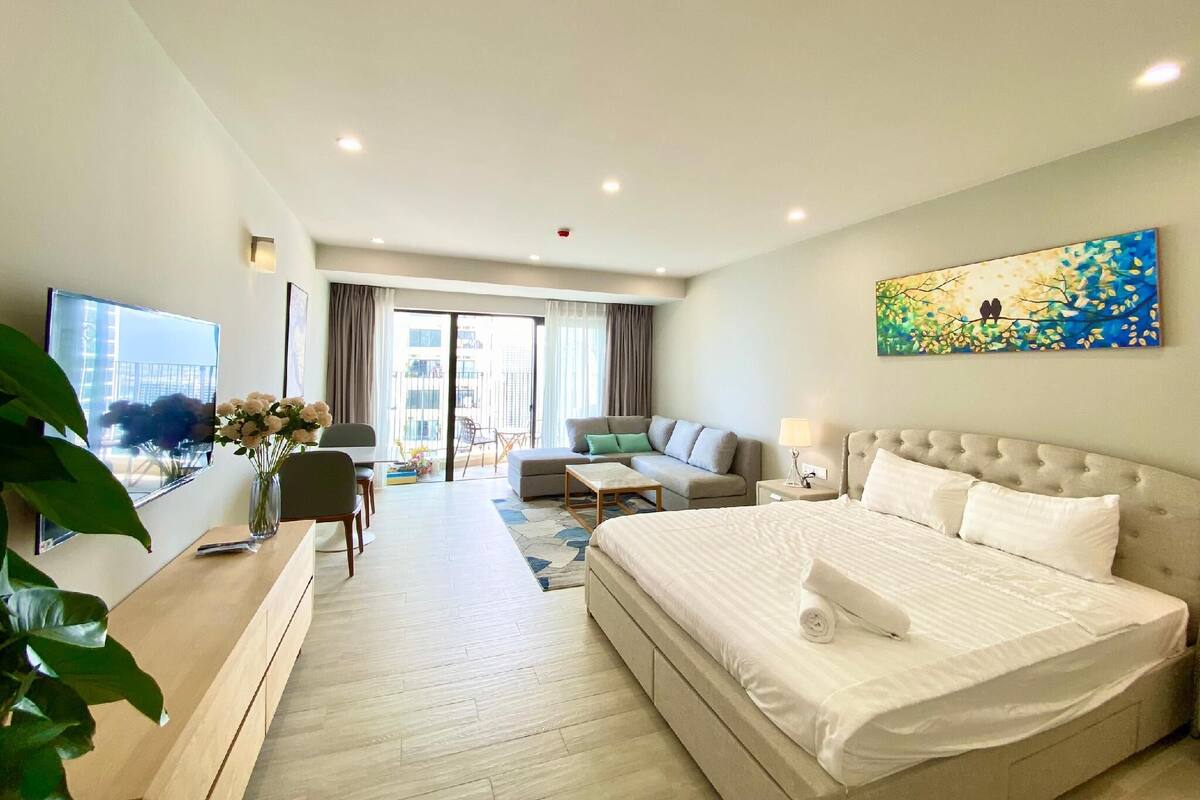 Ein Hotelzimmer mit einem großen Bett, einer Couch, einem Schreibtisch und einem Fernseher. Es gibt einen Balkon mit Blick auf Gebäude.