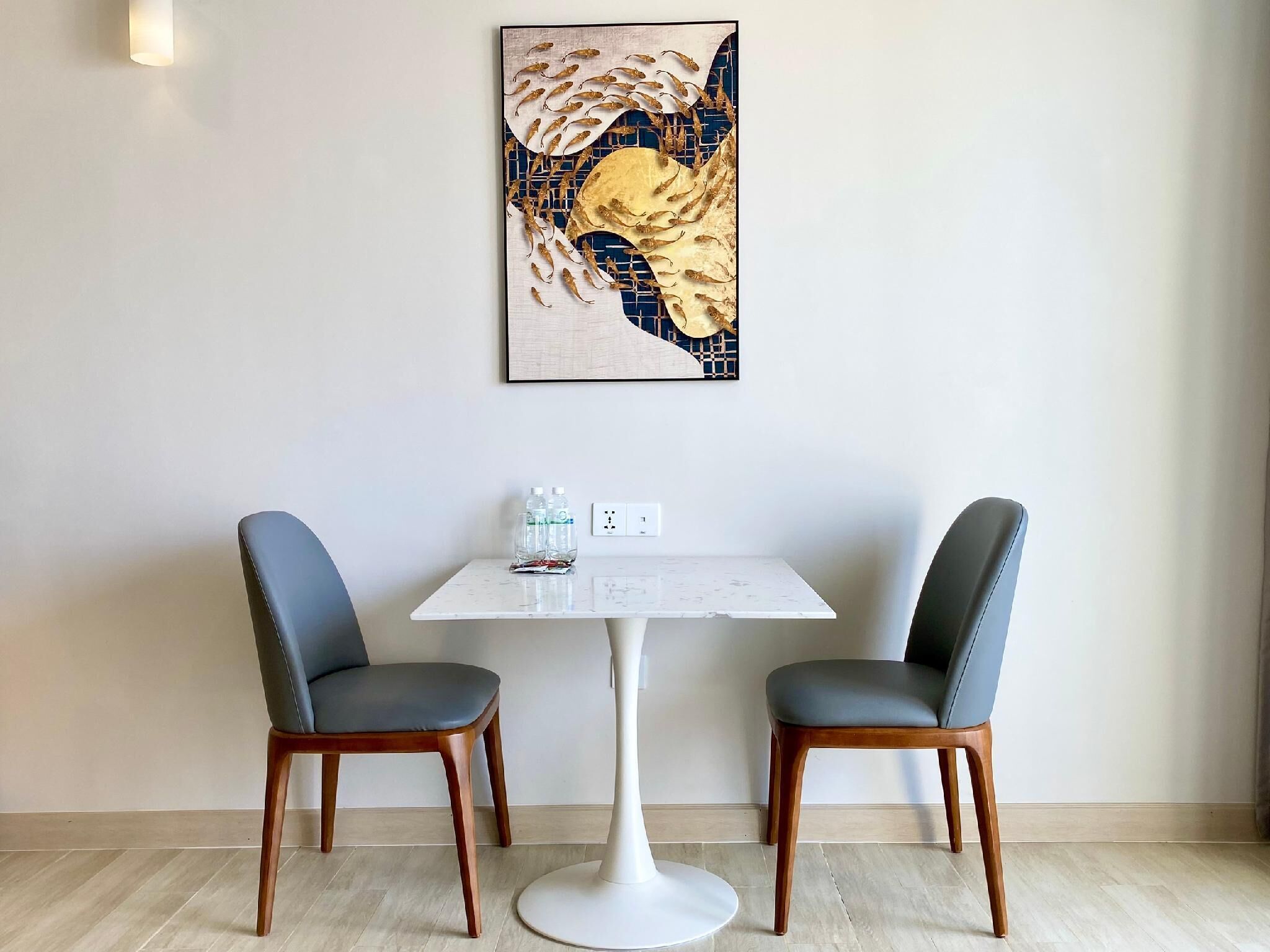 A dining area with a white table and two chairs, a framed artwork above the table, and a small table with bottled water.