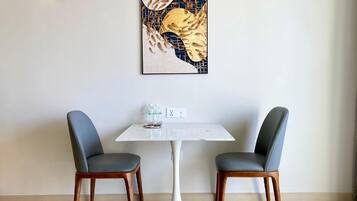 A dining area with a white table and two chairs, a framed artwork above the table, and a small table with bottled water.