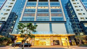 Um hotel moderno com uma placa chamativa de "GOLDCOAST", amplas janelas de vidro e uma entrada bem iluminada.