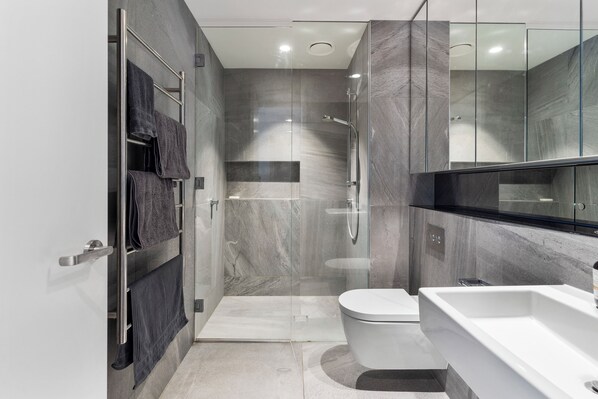 Un baño moderno con cabina de ducha de vidrio, inodoro blanco y un lavamanos grande de color blanco.