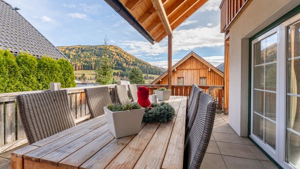 A wooden deck with a table and chairs, a red chair, and a potted plant. - Exclusive chalet with sauna and cinema seats (Mauterndorf)