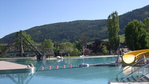 A swimming pool with a slide, a wooden bridge, and a mountainous backdrop. - Exclusive chalet with sauna and cinema seats (Mauterndorf)