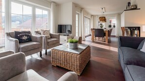 A spacious living room with a large window, a television, a dining area, and a sofa. - Exclusive chalet with sauna and cinema seats (Mauterndorf)