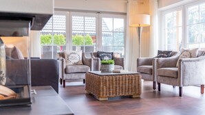 A modern living room with grey armchairs, a wicker coffee table, and a large window with a view of greenery outside. - Exclusive chalet with sauna and cinema seats (Mauterndorf)