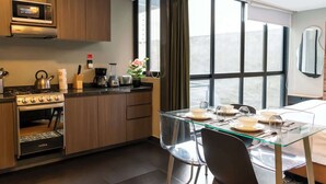 Cocina moderna con microondas, estufa y horno integrados. Cuenta con un comedor con mesa de vidrio y sillas, y un amplio ventanal con cortinas.
