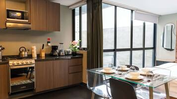 A modern kitchen with a built-in microwave, stove, and oven. There is a dining area with a glass table and chairs, and a large window with curtains.