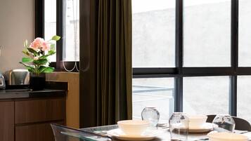 A dining area with a table set for four, a vase with flowers, and a view through large windows.