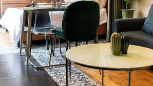 Una habitación de hotel moderna con una cama, una mesa de comedor con sillas, una pequeña mesa redonda, una silla verde, un sofá, una planta en maceta y una pared decorativa con platos.