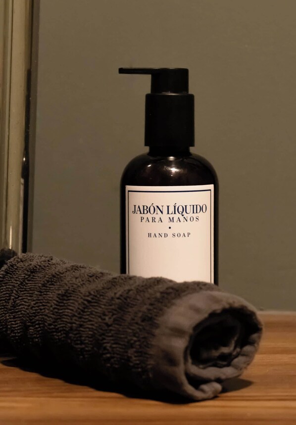 Una botella de jabón para manos con dosificador y una toalla enrollada sobre una superficie de madera.