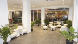 Um saguão moderno com sofás brancos, plantas em vasos e entrada de vidro.