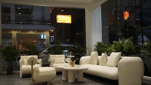Uma sala de estar moderna com um sofá, poltronas e uma mesa de centro. Há plantas em vasos e um carro estacionado na rua.