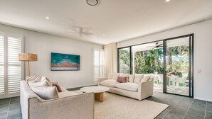 Ein modernes Wohnzimmer mit einem beigefarbenen Sofa, einem runden Couchtisch und einem großen Fenster mit Blick ins Grüne.