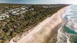 Luftaufnahme einer Küstenlandschaft mit Sandstrand und einer Wohngegend mit Häusern.