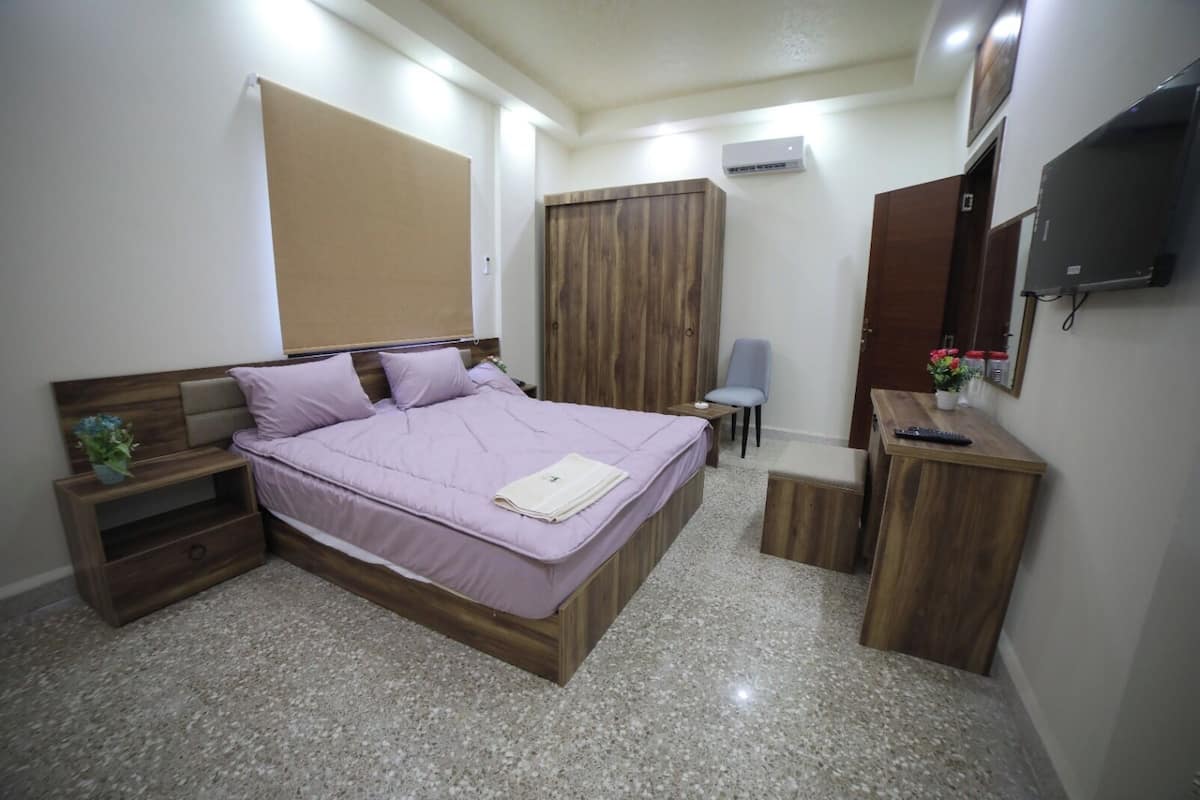 A bedroom with a bed, a nightstand, a desk, a chair, a wardrobe, and a TV.