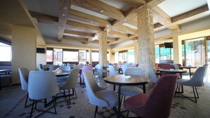 A spacious indoor dining area with multiple tables and chairs, high wooden beams on the ceiling, and large windows allowing natural light. - Village Boutique Hotel (Khenchara)