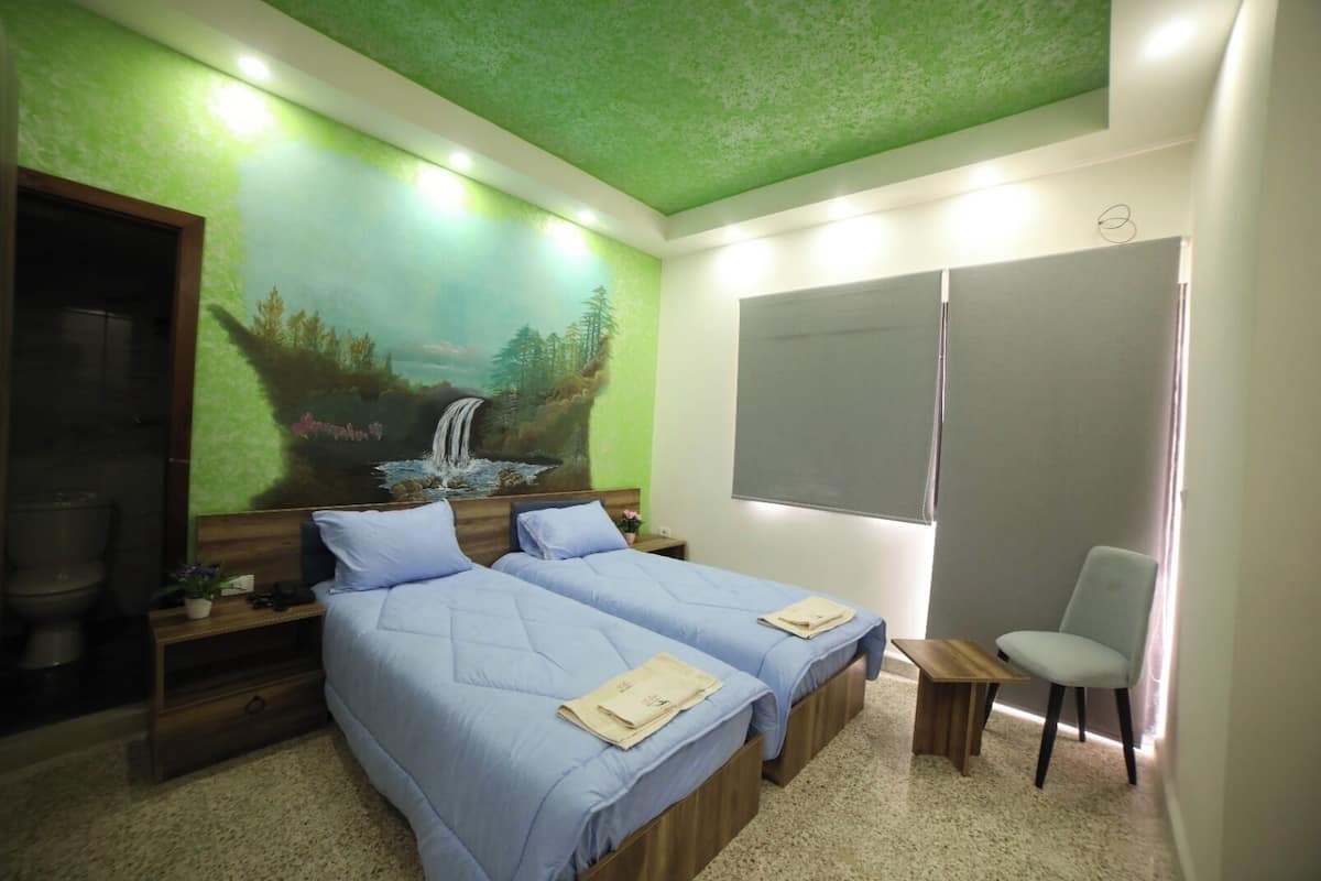 A bedroom with two beds, a wooden nightstand, a small table, and a chair.