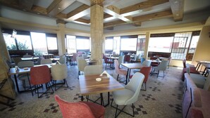 A spacious dining area with multiple tables and chairs, large windows, and a high ceiling with exposed beams. - Village Boutique Hotel (Khenchara)