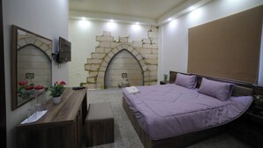 A bedroom with a bed, a desk, a mirror, and a stone wall with a window. - Village Boutique Hotel (Khenchara)