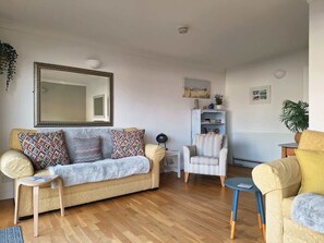 Een woonkamer met een bank, fauteuils, een salontafel, een boekenkast en een spiegel.