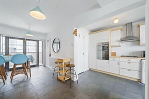Una cocina moderna con armarios blancos, estufa y microondas. Hay un comedor con mesa y sillas.