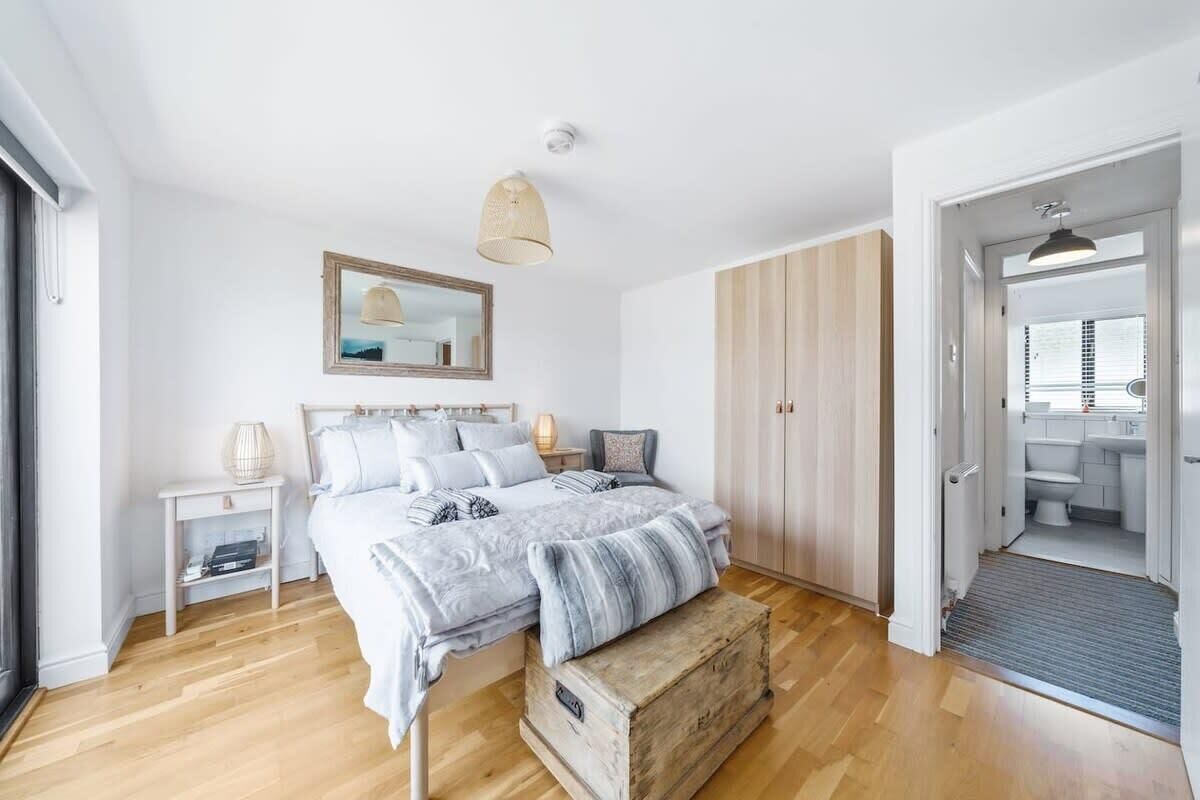 Une chambre à coucher comprenant un lit, des tables de chevet, un miroir, un luminaire suspendu et donnant sur la salle de bain.