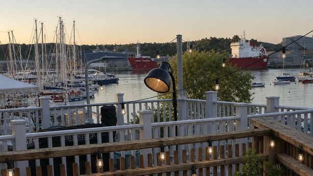 En terrasse med en fletsofa, to små runde borde og gelænder med lyskæder.