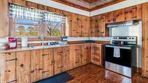 A kitchen with wooden cabinets, a stainless steel stove, and a window with a plaid valance.